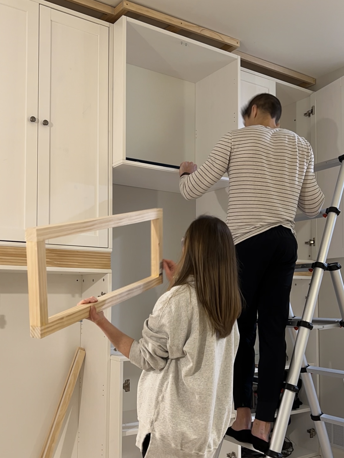 Man and woman leveling and attaching cabinets.