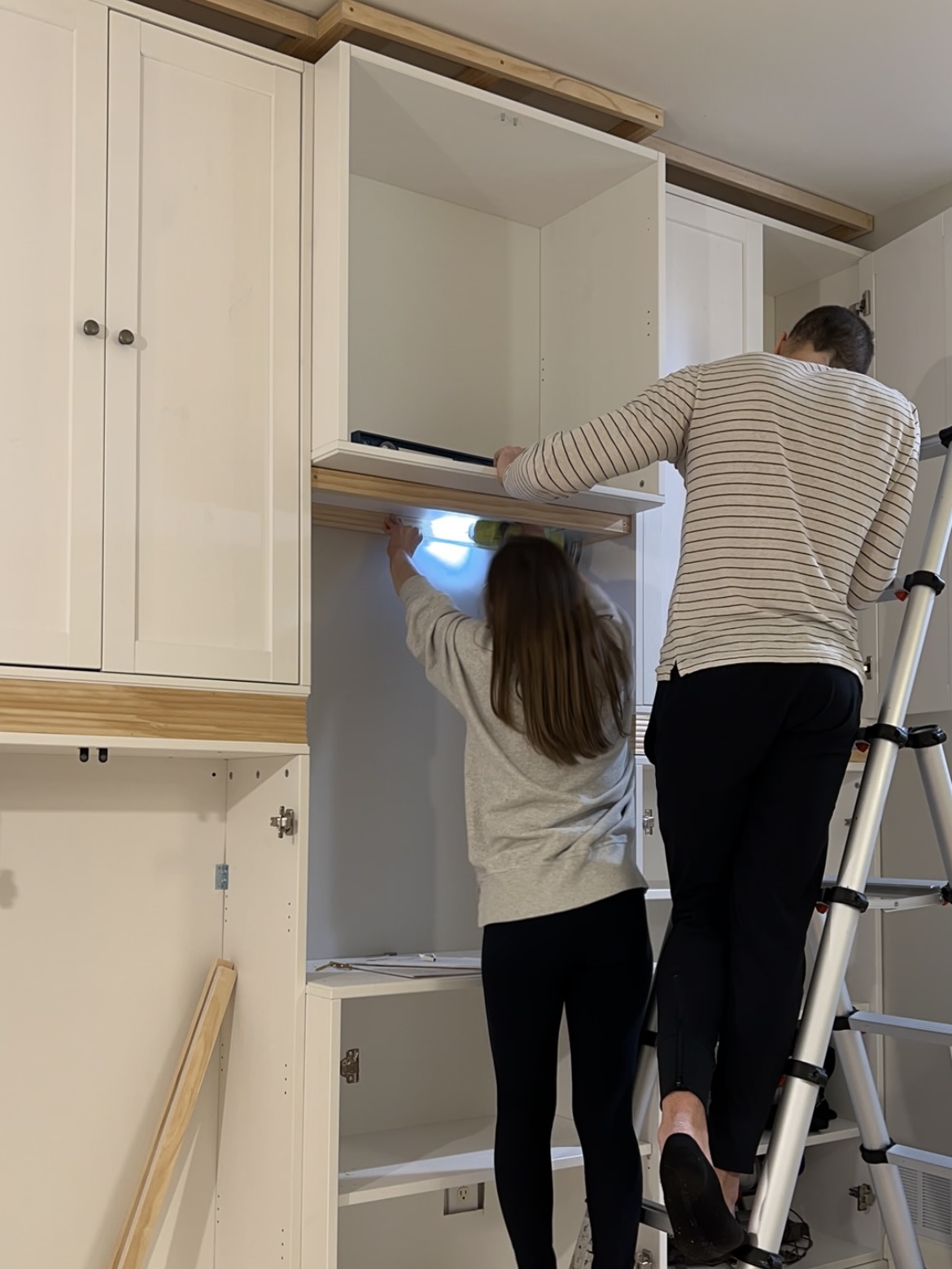 Man and woman leveling and attaching cabinets.