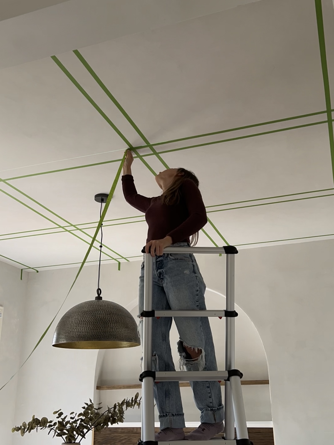 Woman on a ladder taping lines on a ceiling.