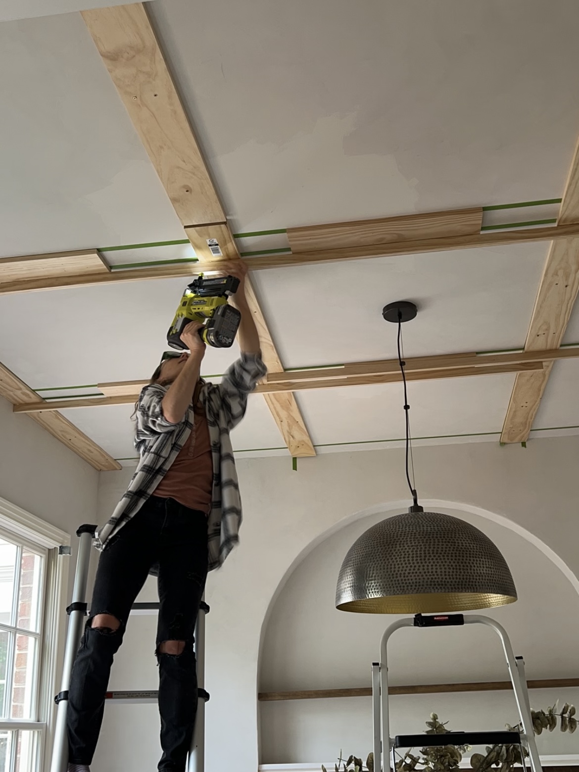 Woman attaching1x6 boards to the ceiling in a grid pattern, using a nail gun.