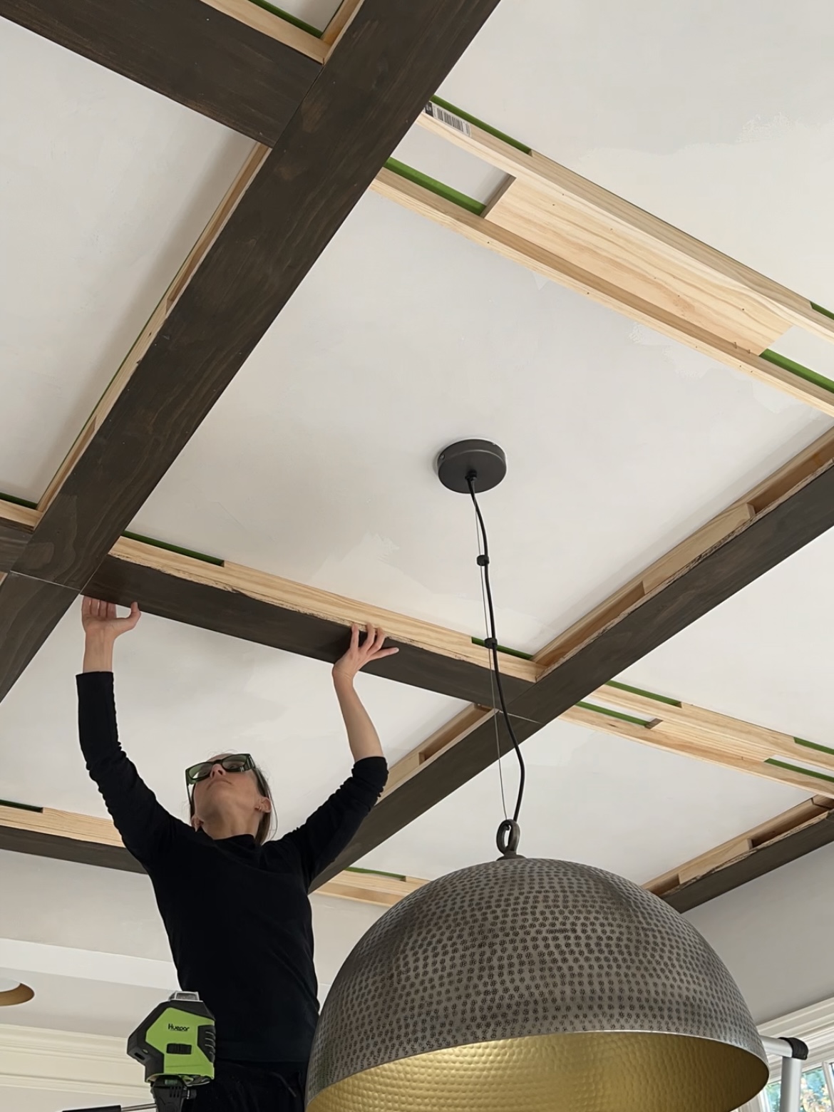 Woman aligning a stained board on a wooden grid attached to a ceiling.