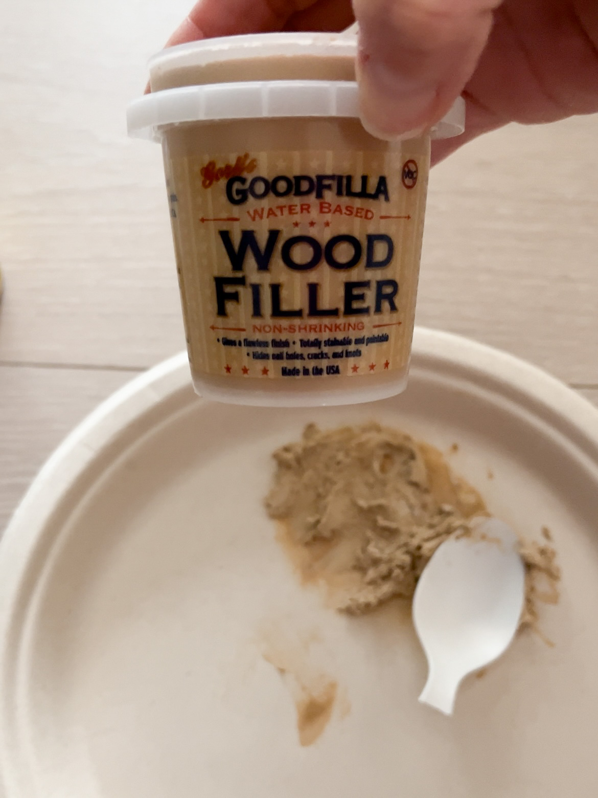 Hand holding a tub of Goodfilla Wood Filler.
