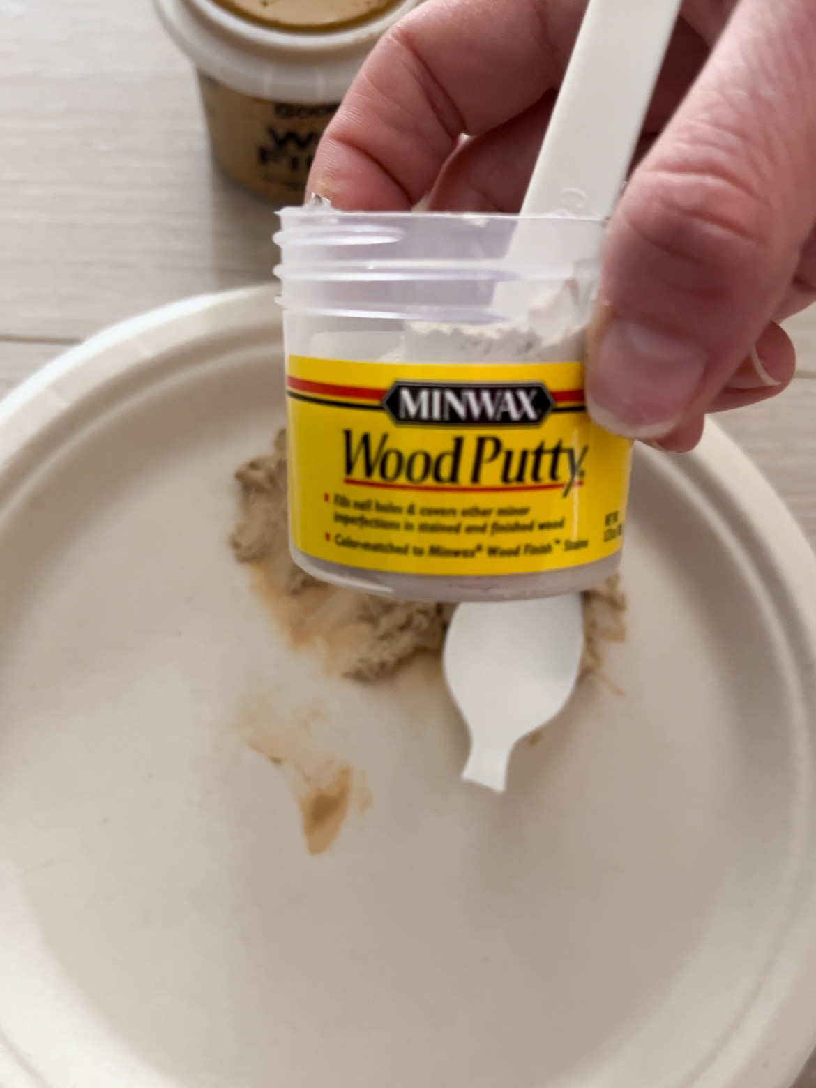 Hand holding a tub of Minwax Wood Putty.