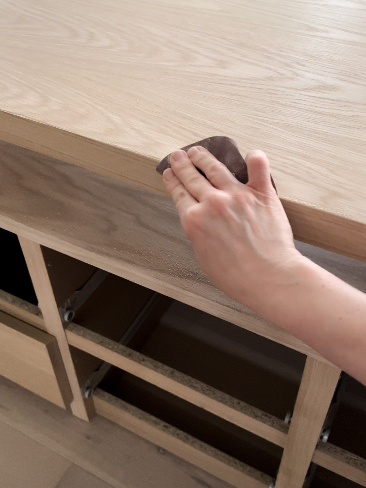 A hand sanding the edge of the furniture 