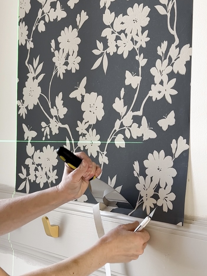 Using a putty knife and xacto knife to trim wallpaper excess at the trim.