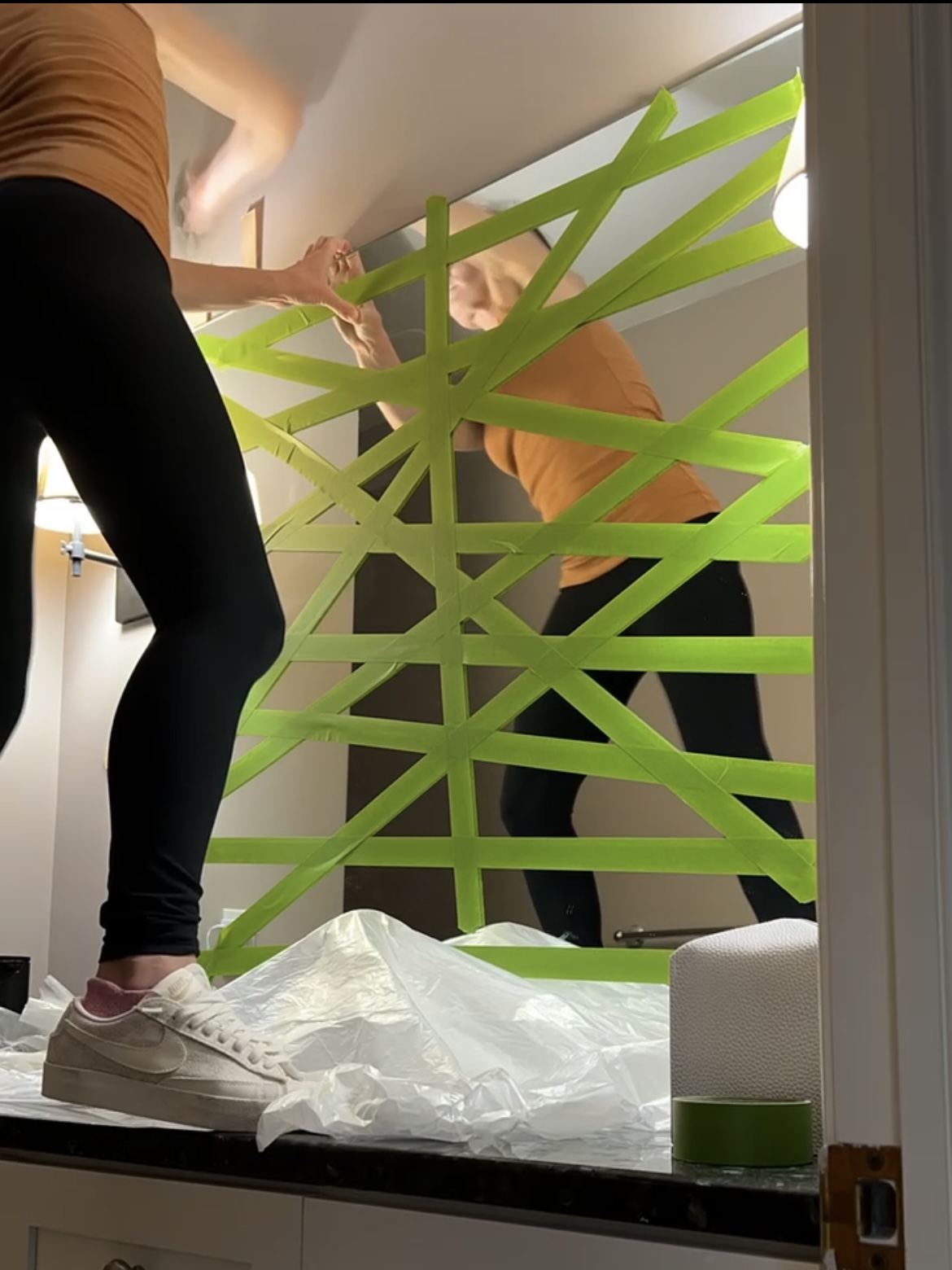 Woman removing mirror from wall. Mirror is crisscrossed with green tape.