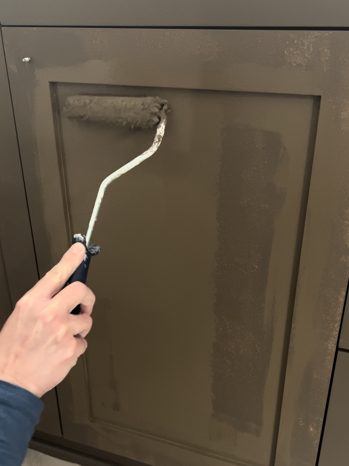 Rolling brown paint onto a bathroom vanity cabinet door.