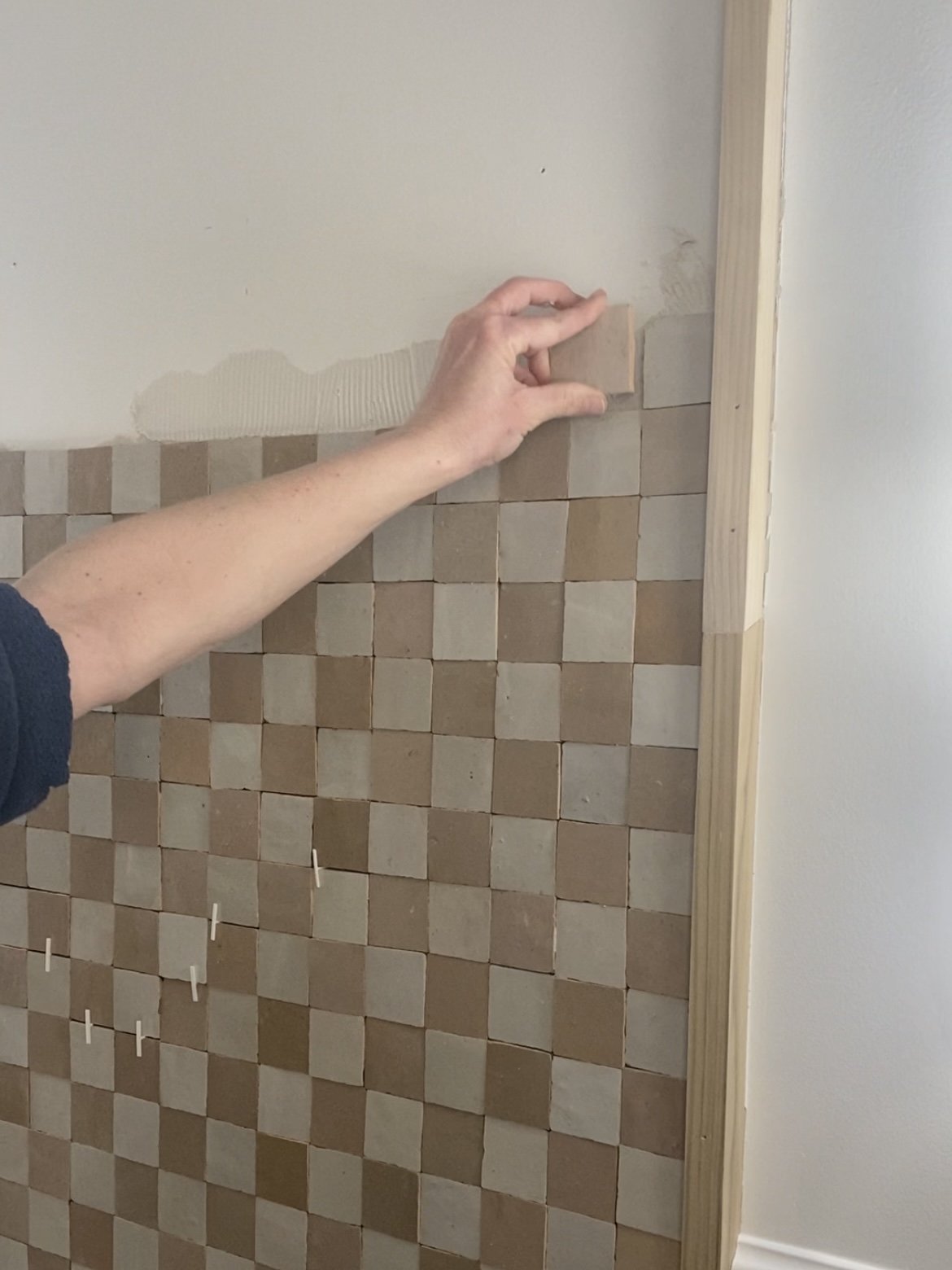 Placing a square of Zellige tile onto the wall in a checkerboard pattern.