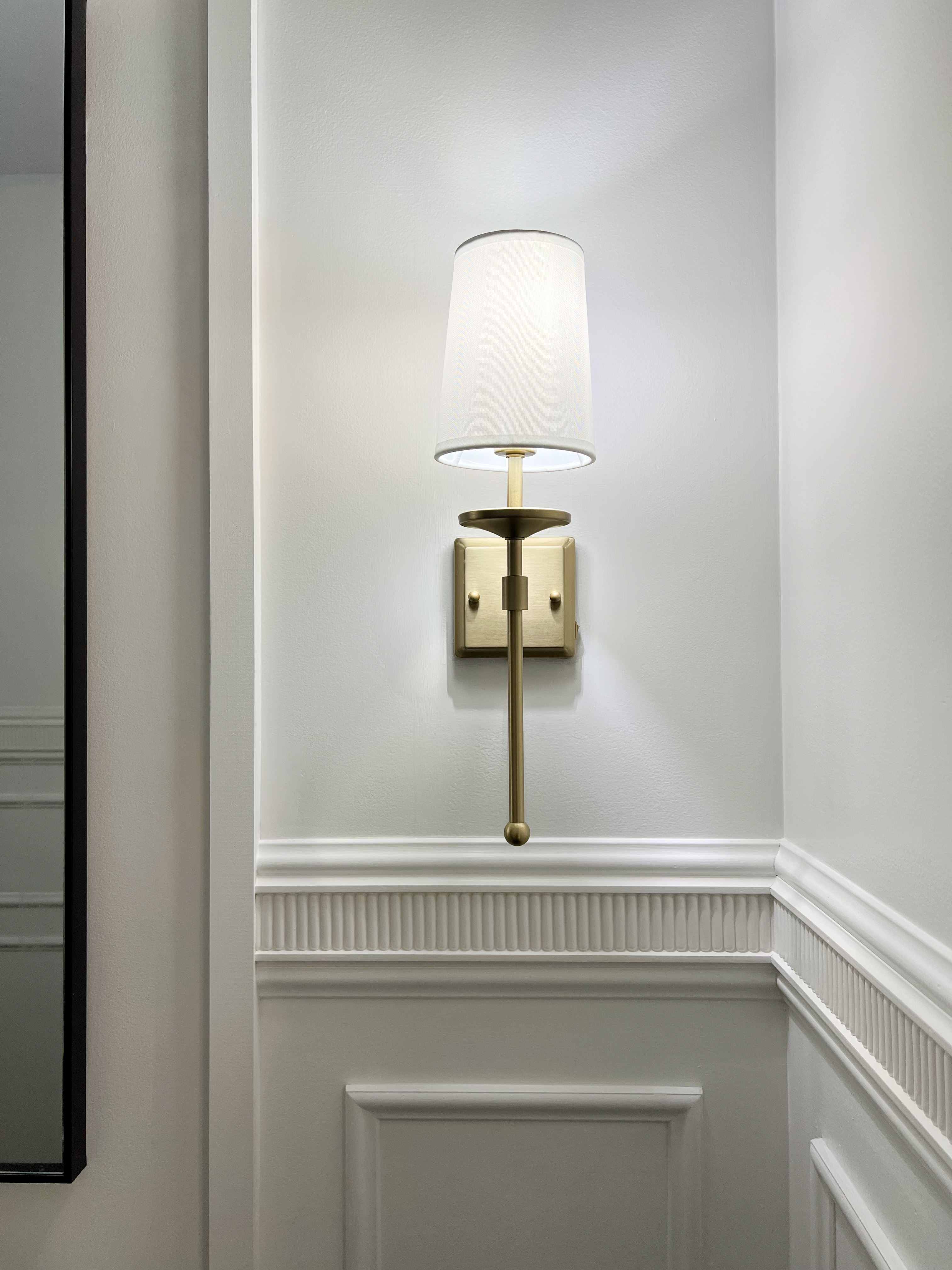 Brass light sconce on bathroom wall above ornate wall trim.