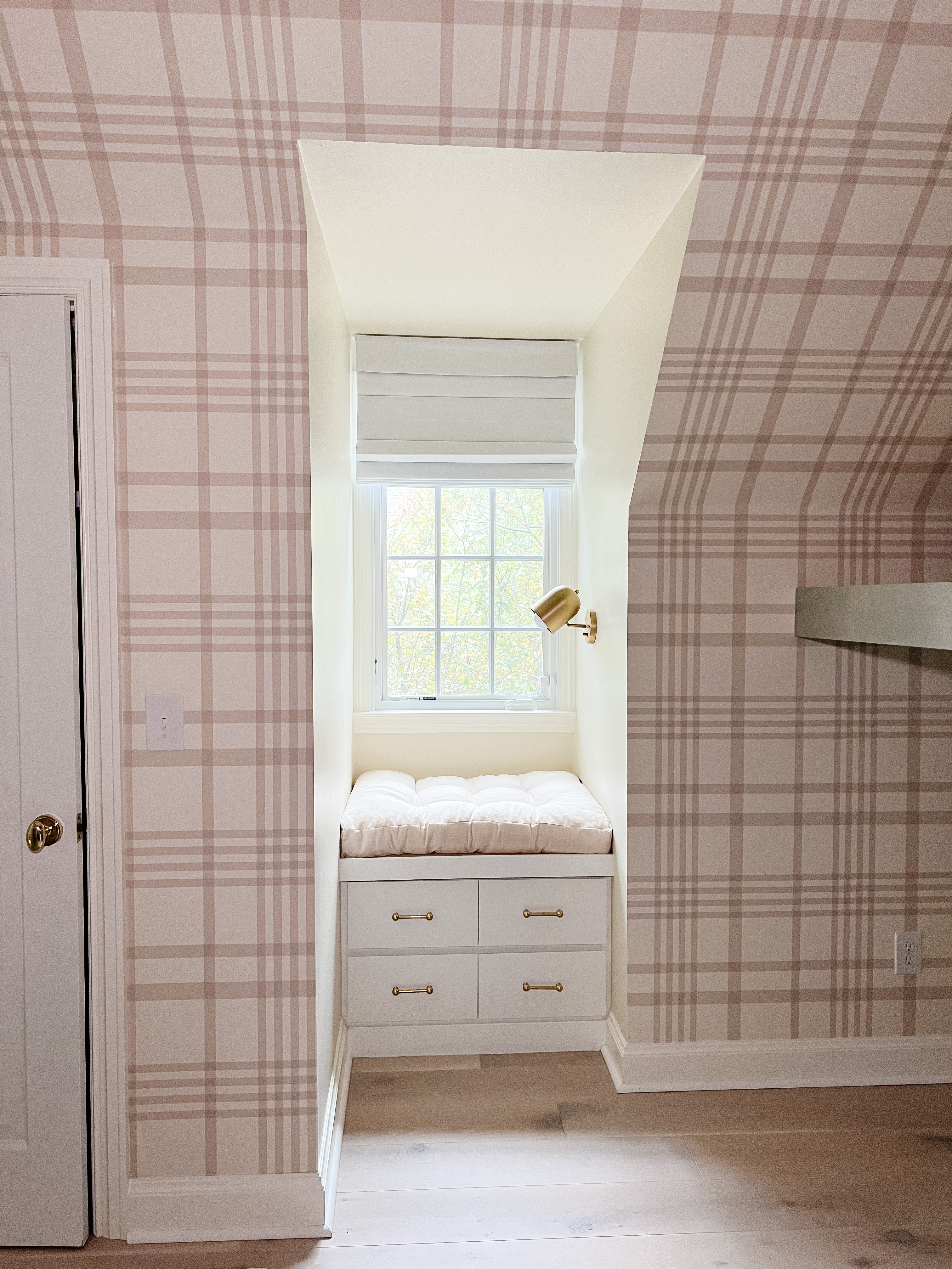 Window seat with four drawers in a dormer window of a room with plaid wallpaper.