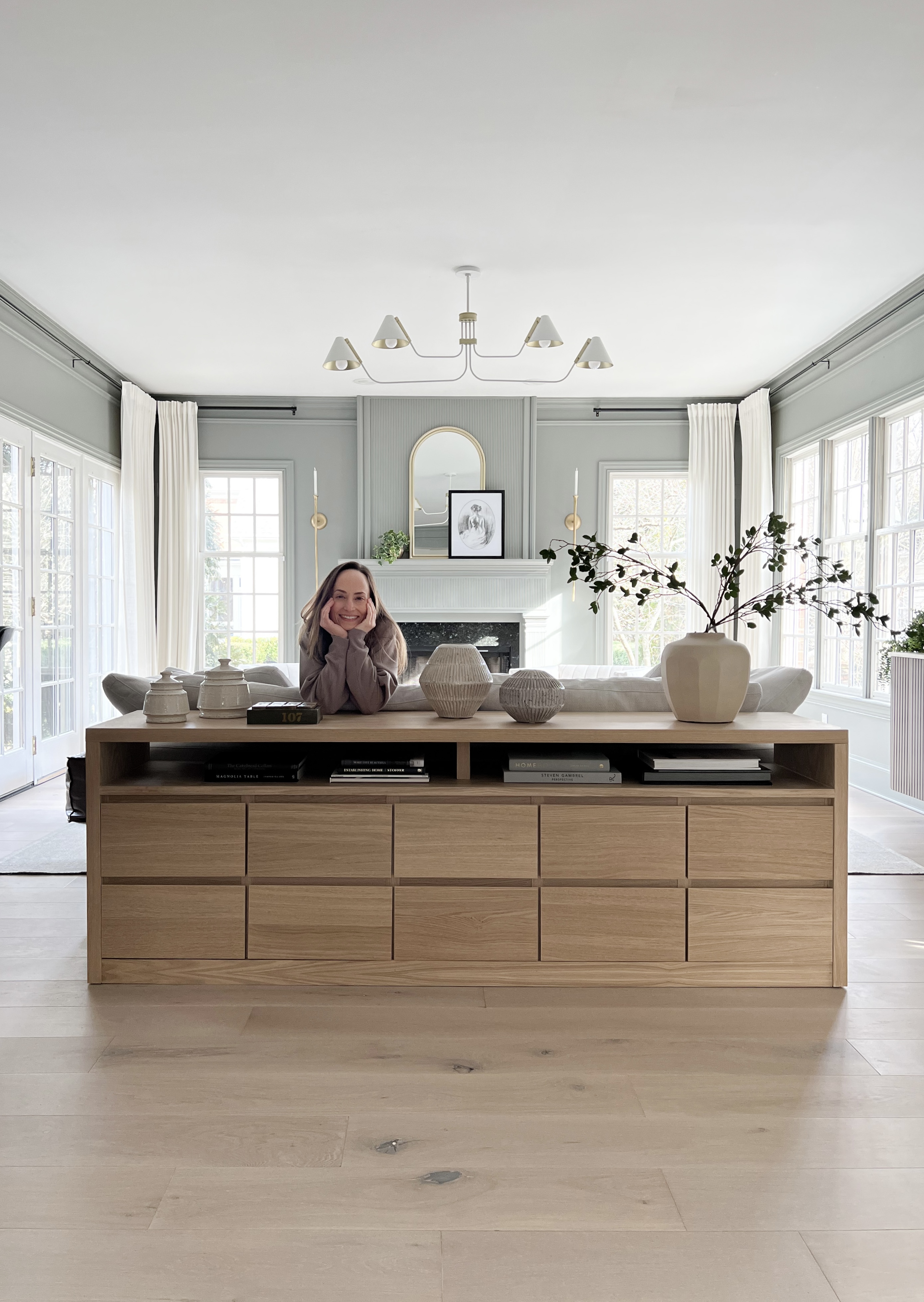 An extra large sofa table in an airy living room, with a woman behind it. The sofa table was created using an IKEA nightstand hack of using MALM nightstands for the drawer portion of the build.