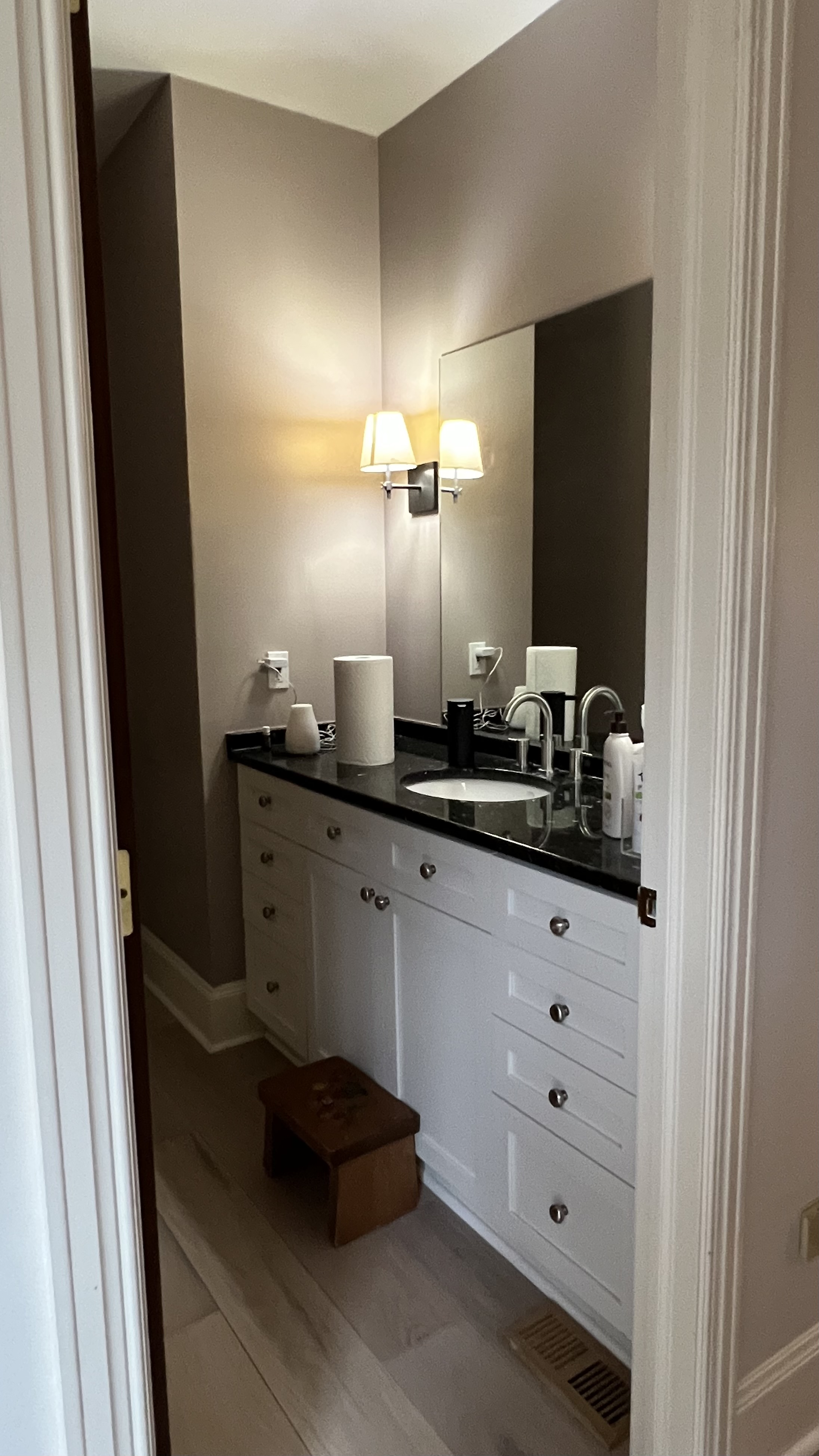 Photo of a bathroom with a white sink, black countertop, and square mirror.