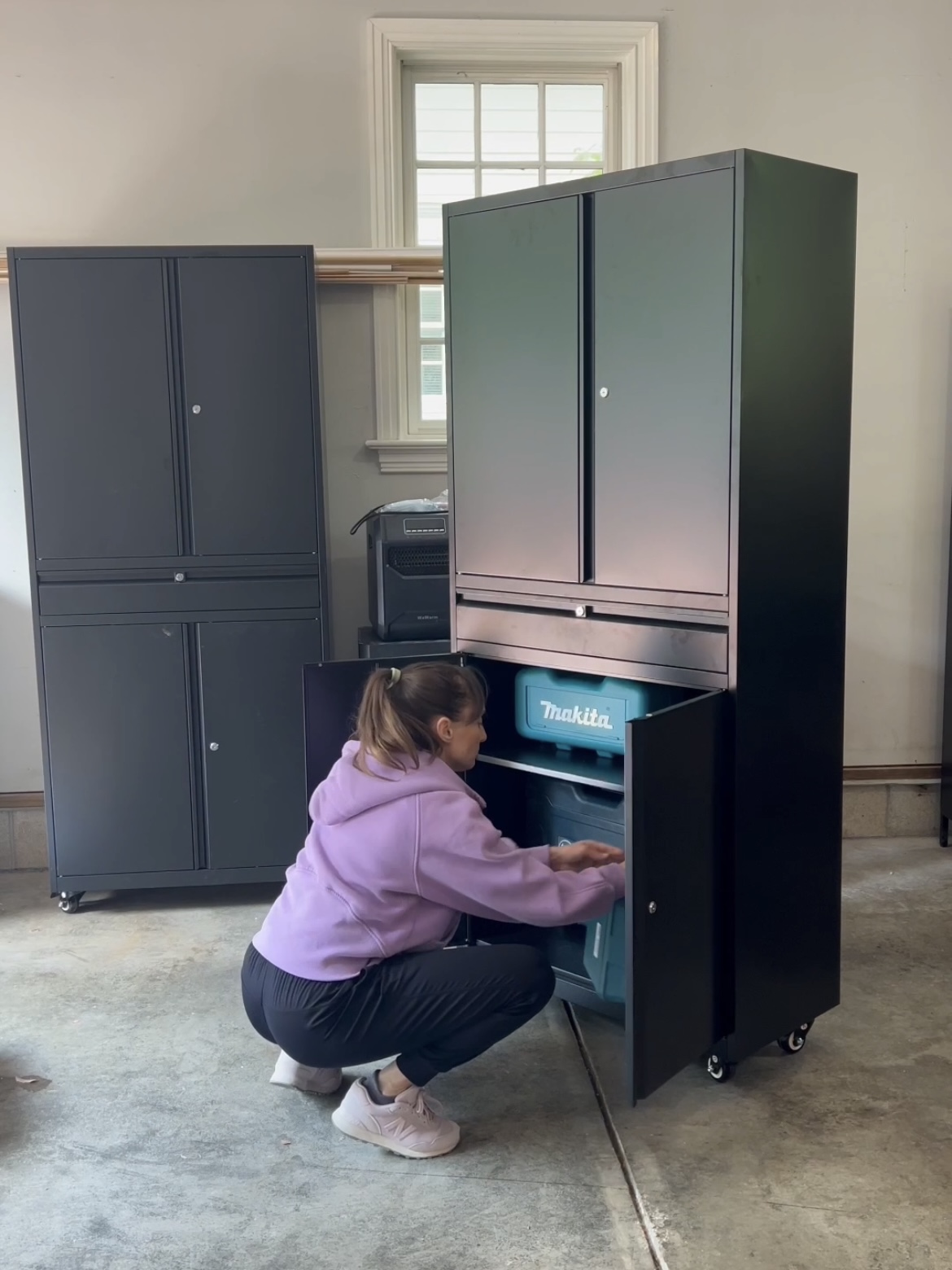 Woman adding tools to a rolling tool cabinet in a garage.