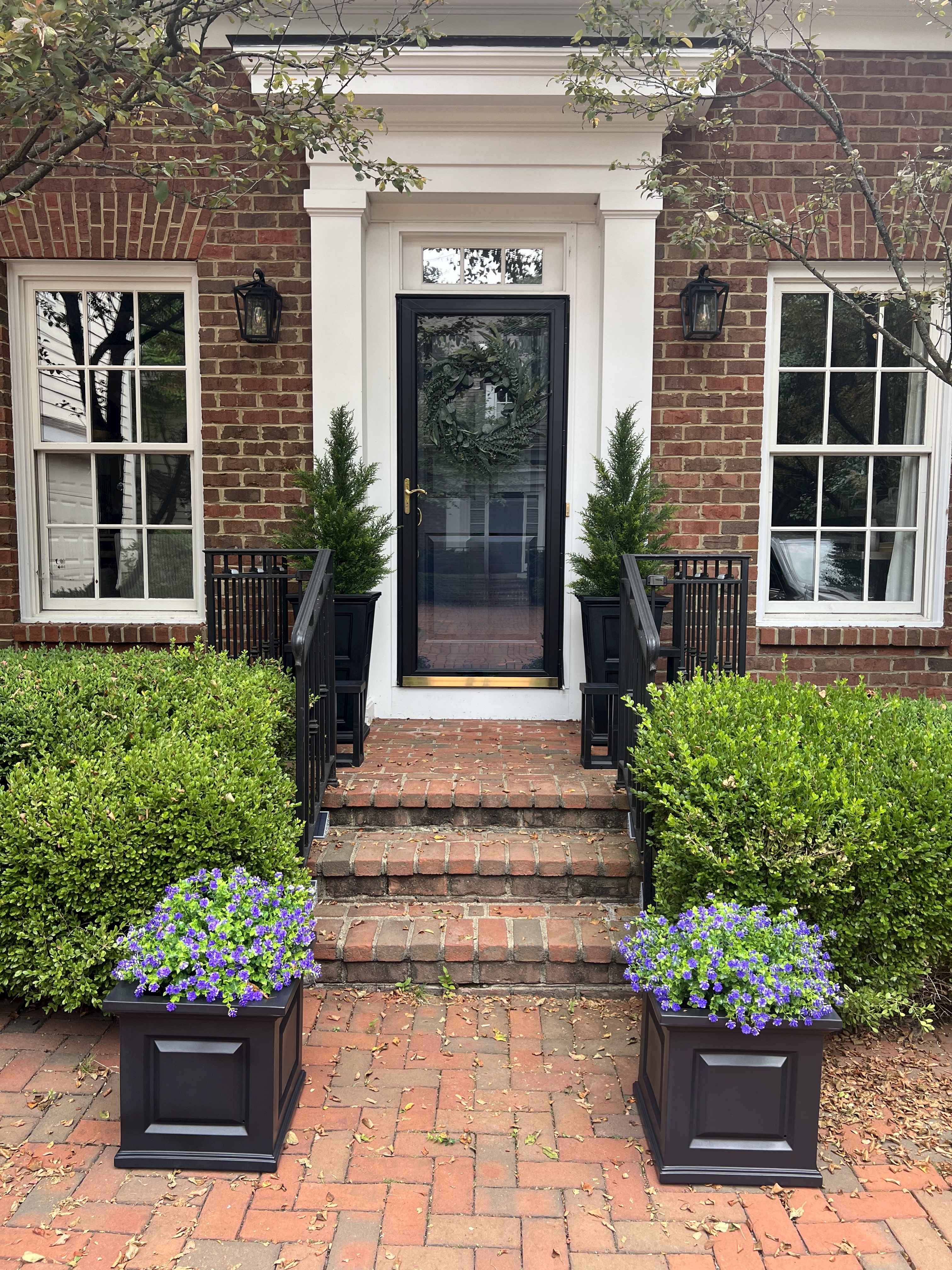 Image of a front porch with several faux plants in a black metal planters.