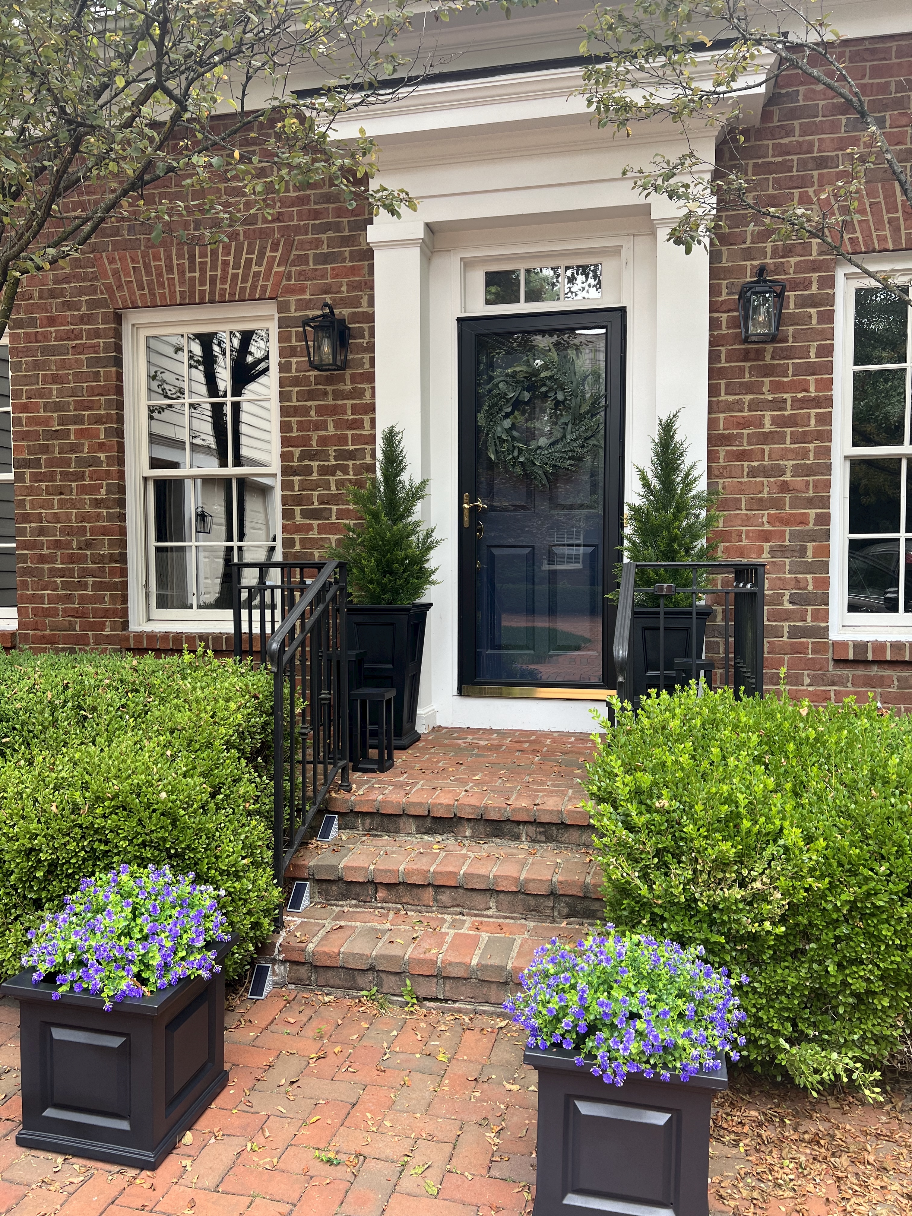 Image of a front porch with several faux plants in a black metal planters.