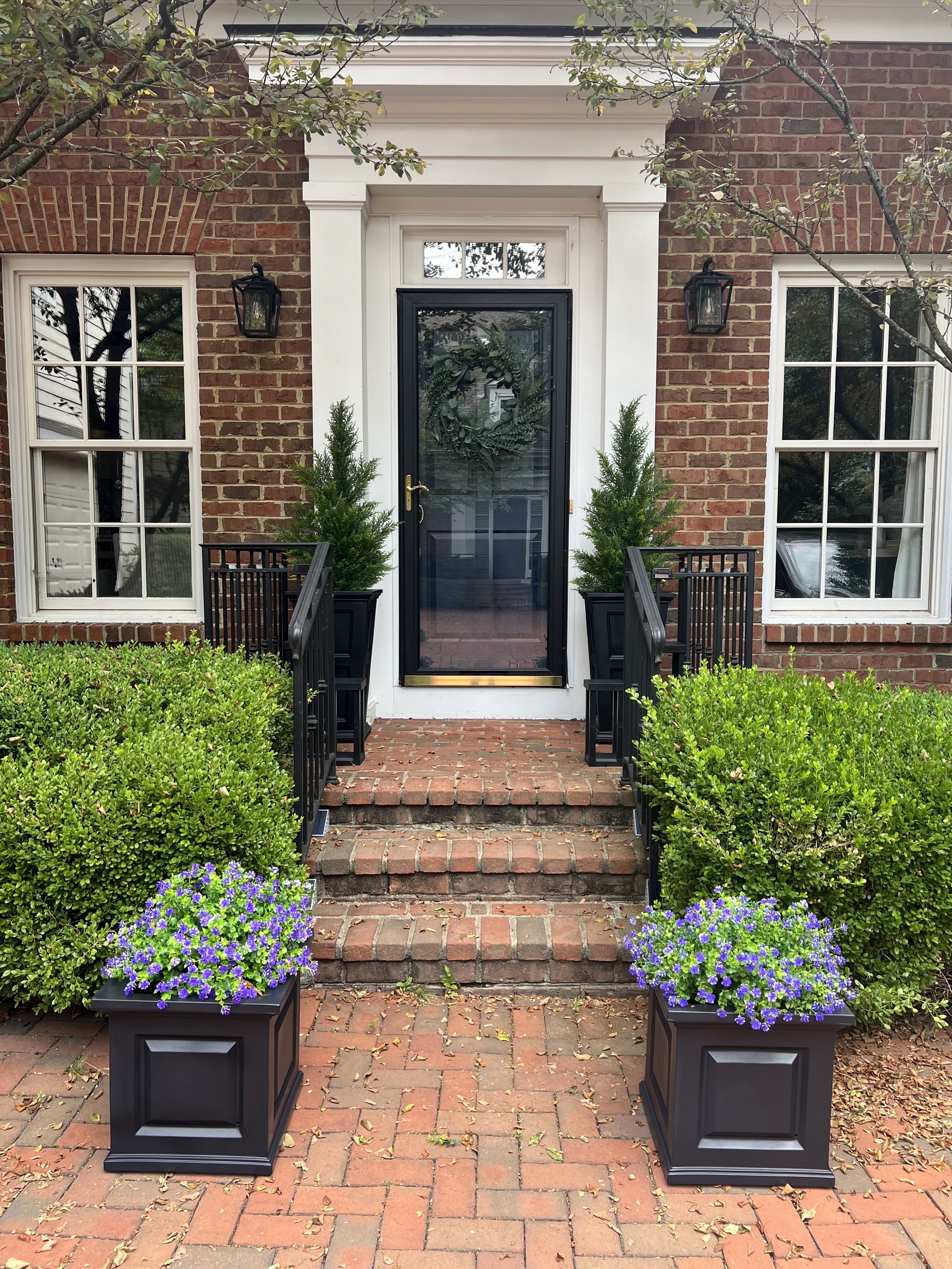 Image of a front porch with several faux plants in a black metal planters.