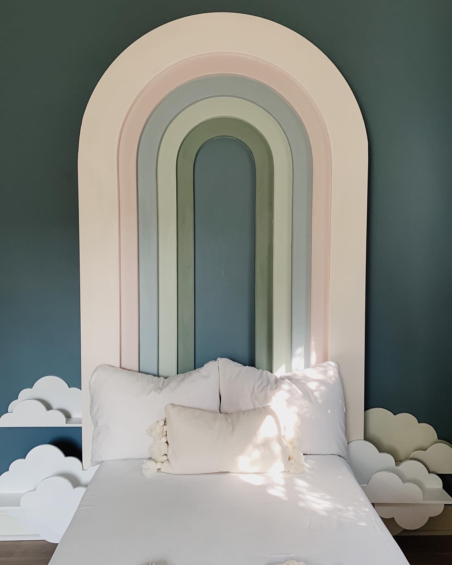 Pastel DIY rainbow headboard above white twin sized bed, with white puffy cloud shelves at bed side level.