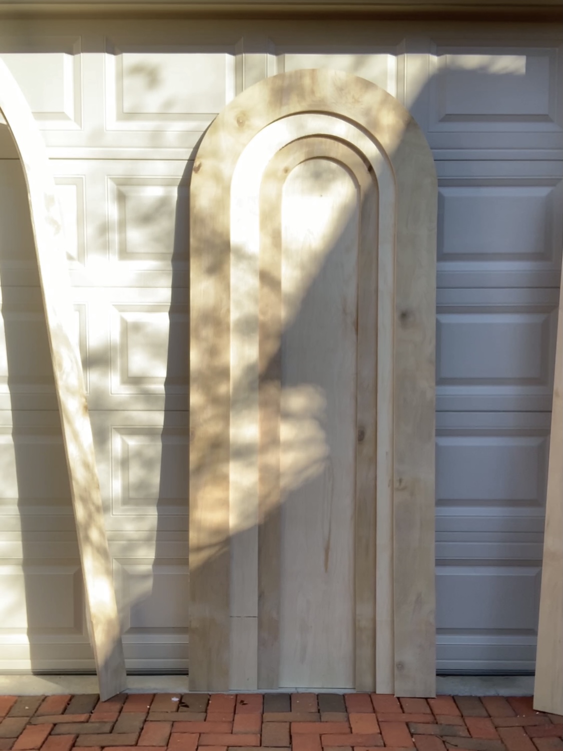 The pieces of a DIY rainbow headboard leaning against a garage door in dappled sunlight.