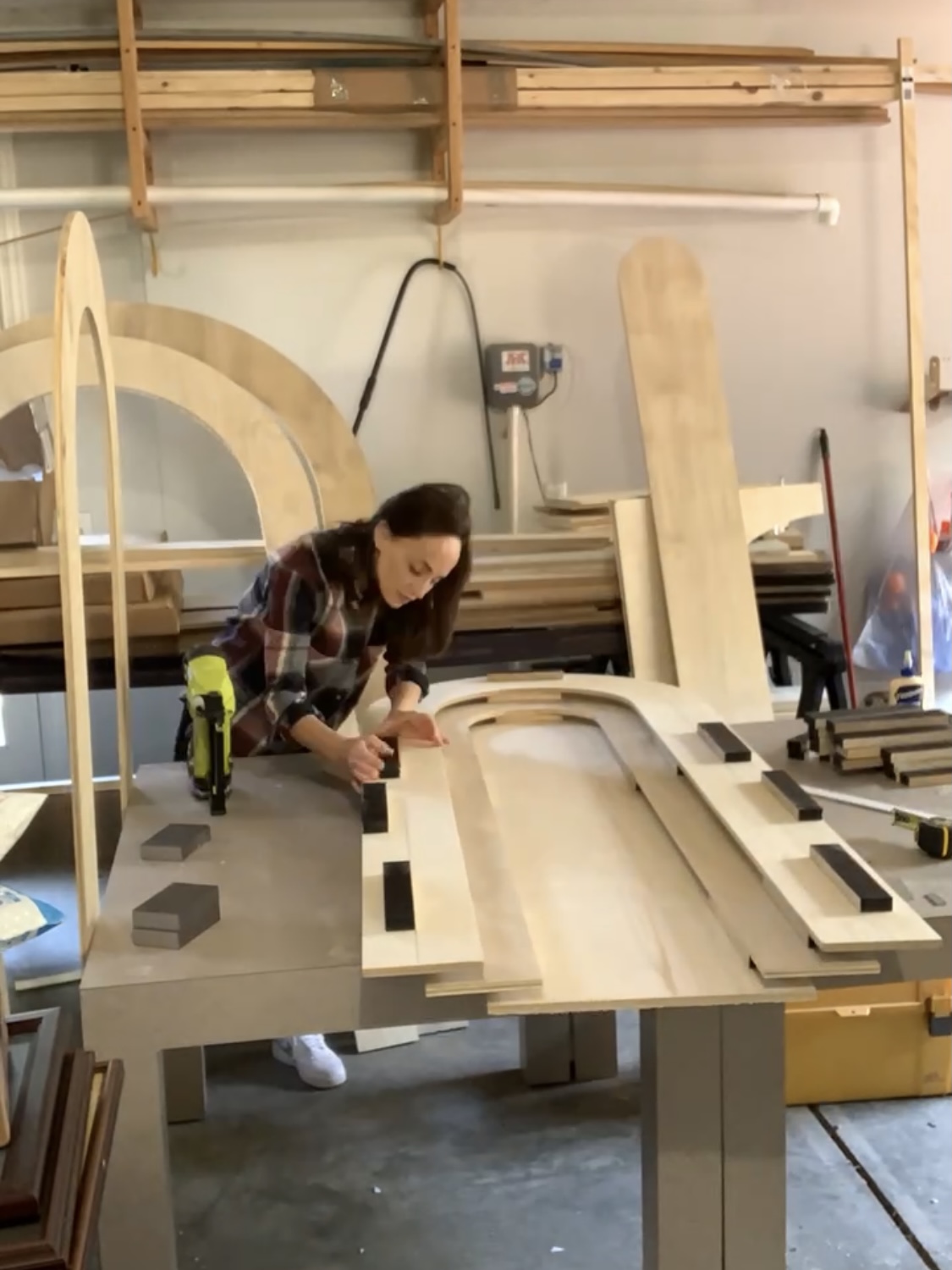 A woman using a nail gun to attach blocking between layers of a DIY rainbow headboard.