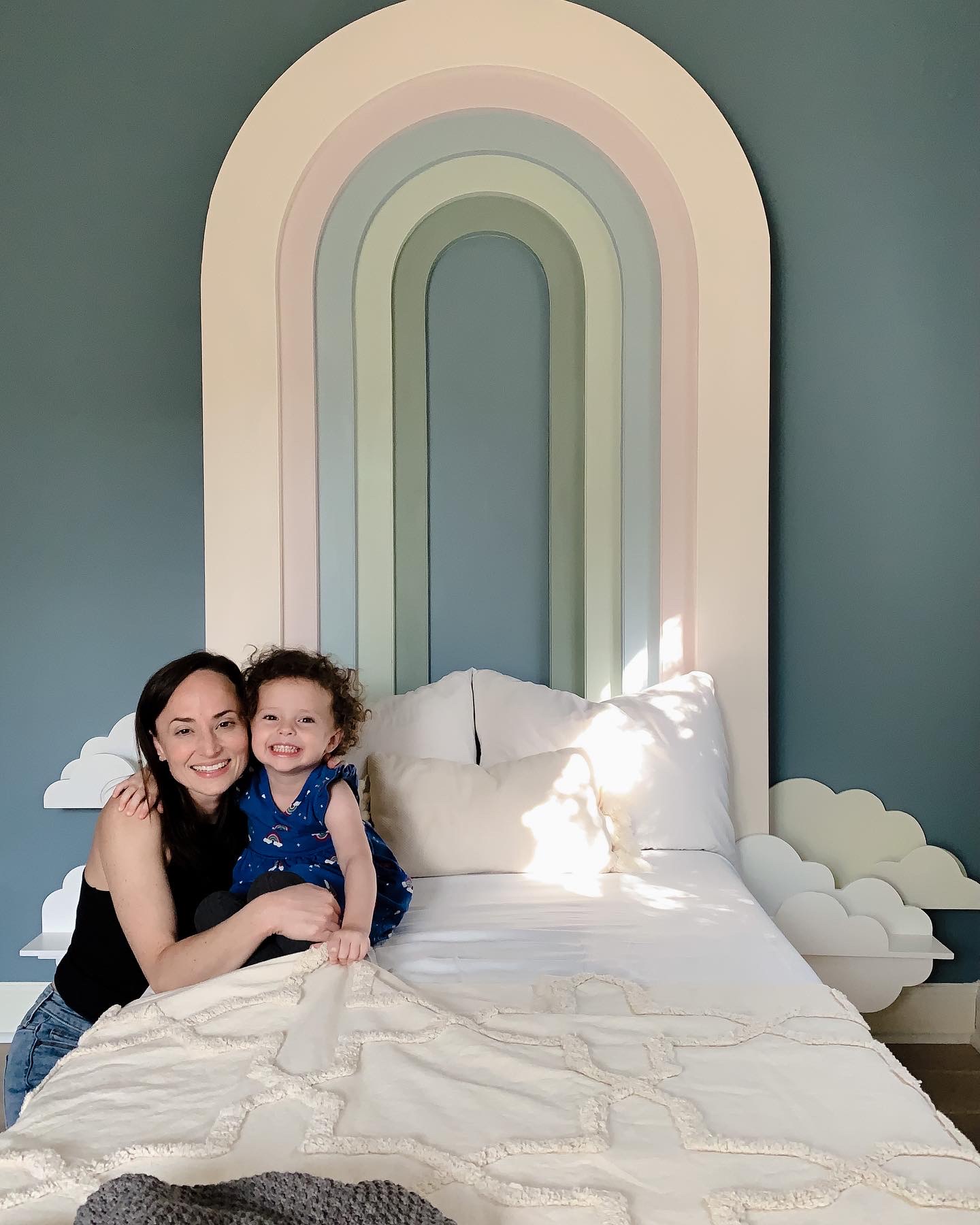 Image of a mother and young daughter hugging on a bed with a diy rainbow headboard.