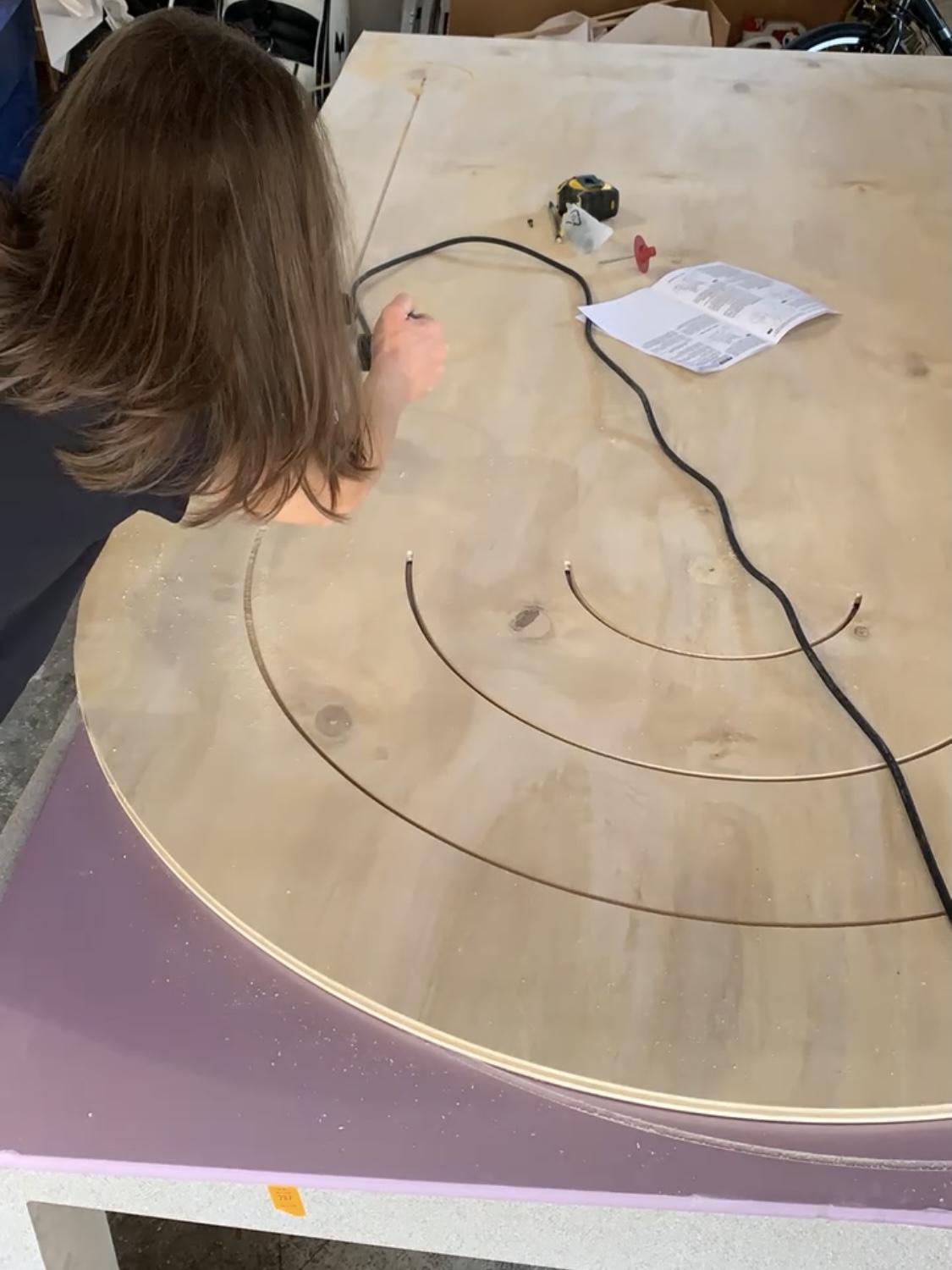 A woman using a router to cut a design in a piece of plywood.