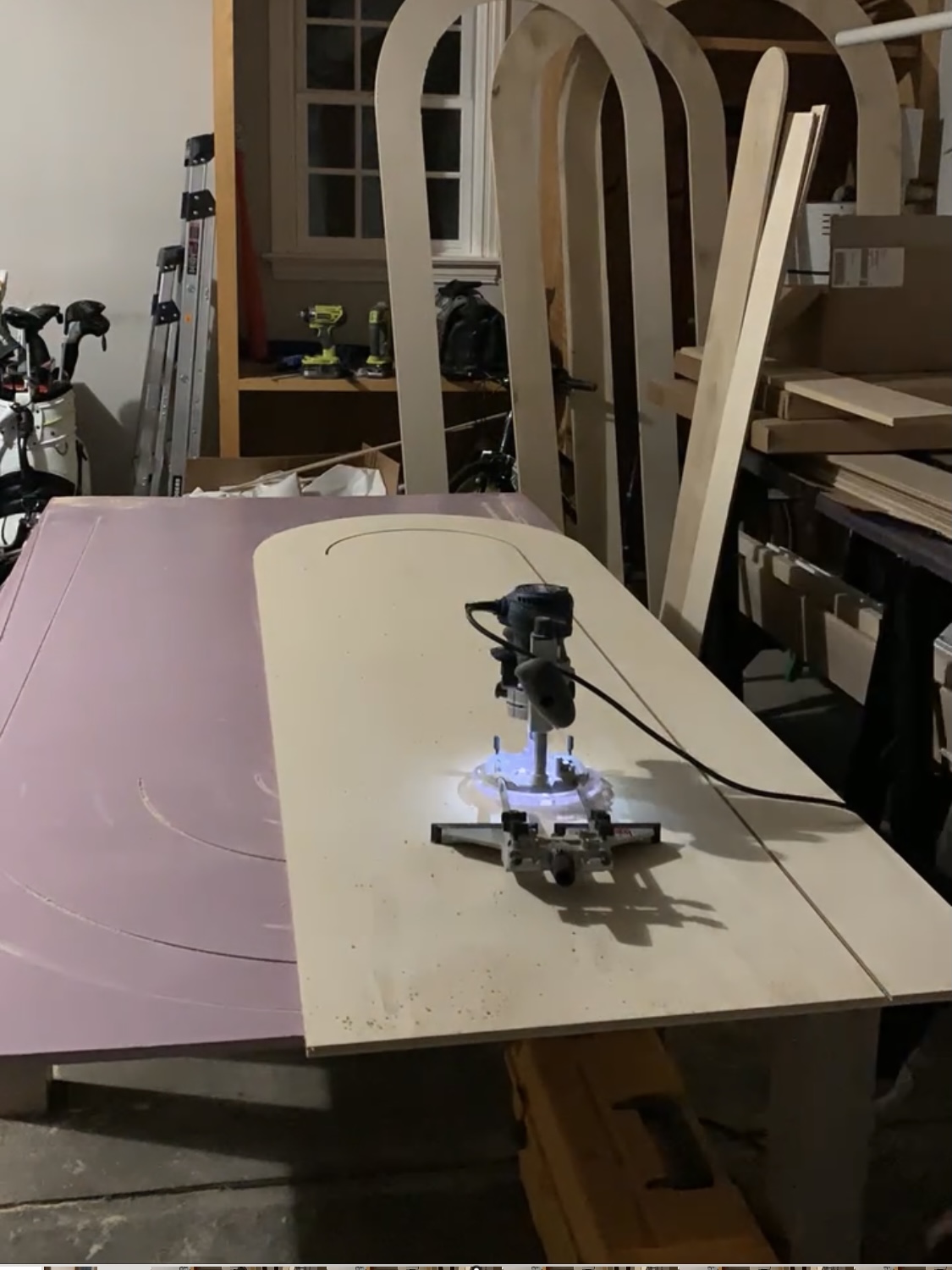 A router sitting on the center of a piece of plywood cut into an arch or rainbow shape.